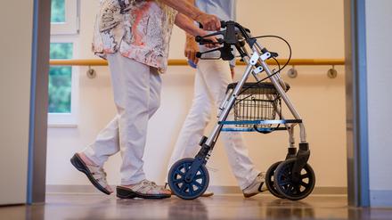 Eine Pflegekraft geht in einem Pflegeheim mit einer älteren Dame mit Rollator über einen Korridor. (Symbolbild)