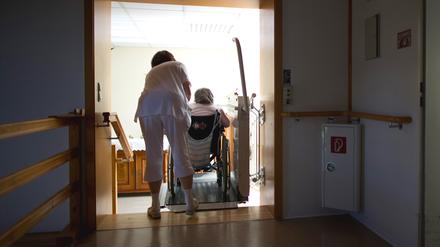 ARCHIV - Eine Pflegerin hilft einer Bewohnerin einer Altenpflegeheimes mit einer Rollstuhlhilfe eine Treppe hinauf, aufgenommen am 26.04.2012. Foto: Arno Burgi/dpa +++ dpa-Bildfunk +++