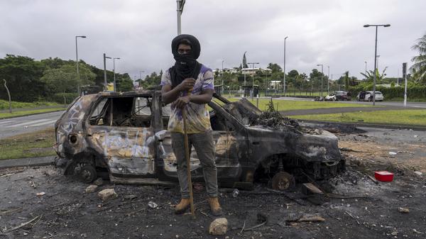 Ein Mann steht vor einem verbrannten Auto nach Unruhen in Neukaledonien.