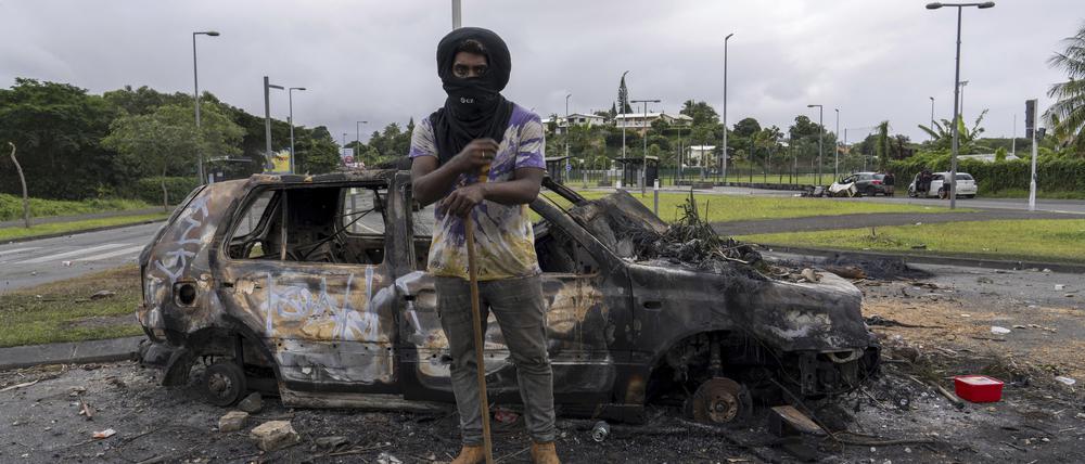 Ein Mann steht vor einem verbrannten Auto nach Unruhen in Neukaledonien.