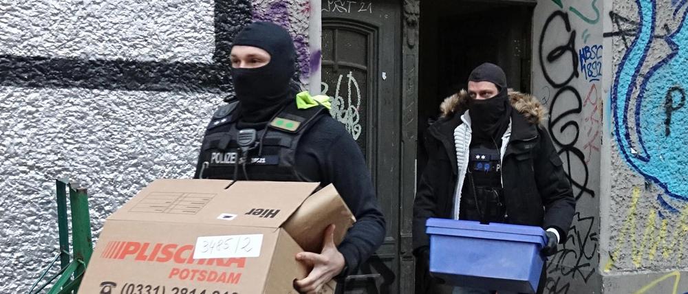 Polizeibeamte tragen während einer Durchsuchungsaktion Kartons aus einem Mietshaus.