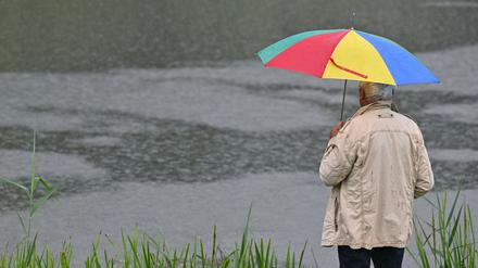 Ein Mann mit Regenschirm steht am Fluss Schwarze Elster. 