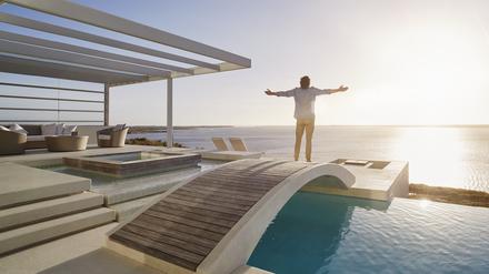 Mann steht auf einer Brücke über seinem Swimmingpool in seiner Luxusvilla und genießt die Aussicht.