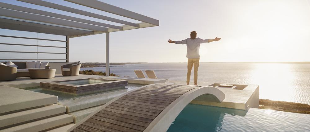 Mann steht auf einer Brücke über seinem Swimmingpool in seiner Luxusvilla und genießt die Aussicht.
