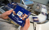 Eine Mitarbeiterin des Schokoladenherstellers Ritter Sport prüft die Verpackung einer Tafel Schokolade.