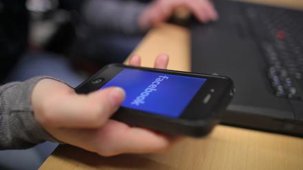 Eine Schülerin hält ein Smartphone mit der öffnenden Anwendung Facebook in der Hand. (Symbolbild)