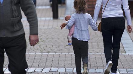 Ein Mädchen mit einer Puppe im Arm geht an der Hand einer Frau durch die Stadt Rotherham.