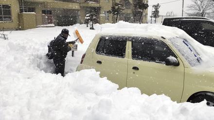 Ein Anwohner schaufelt auf einem Parkplatz in der Stadt Kitami in der Präfektur Hokkaido im Norden Japans den Schnee um ein Auto herum weg.