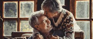 Senior people at home in love kissing and caring each other. Happy relationship mature man and woman together. Old male sitting on the couch and aged woman hugging him with care
