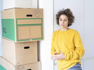 Eine nachdenklich wirkende Frau steht in einer Wohnung neben gepackten Kisten. 