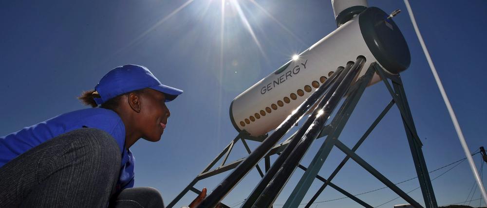 Eine Frau installiert ein Solarwasserheizungsanlage auf dem Dach ihres Hauses in Kuyasa bei Kapstadt  