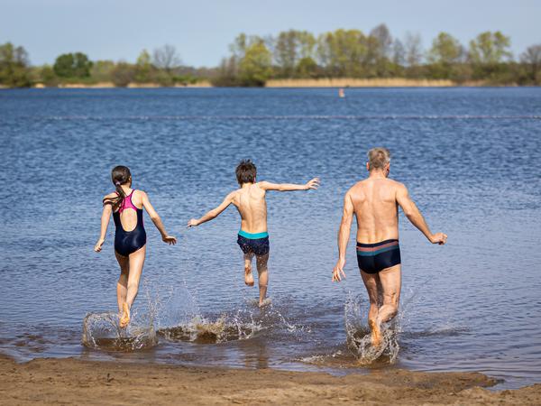Eine Familie läuft bei sonnigem Wetter in den Hufeisensee in der Region Hannover. 