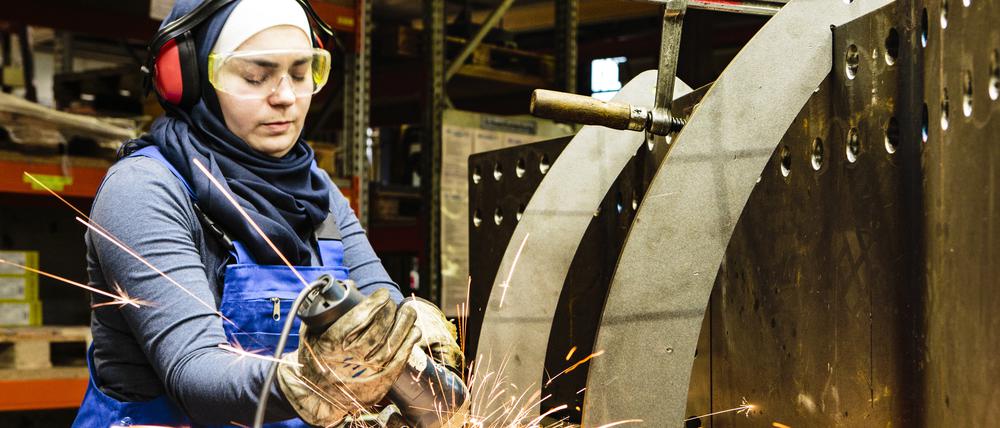 Young female trainee welds steel with grinder in workshop, flying sparks