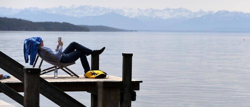 Ein Mann liegt in einem Liegestuhl auf einem Steg am Starnberger See.