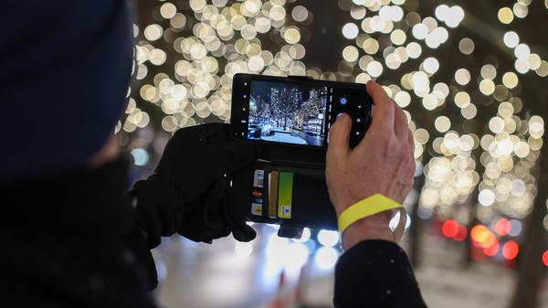 Eine Person fotografiert den Start der Weihnachtsbeleuchtung am Ku’damm an der Grünfeld-Ecke. Mangels Finanzen ist sie weniger opulent als in anderen Jahren.