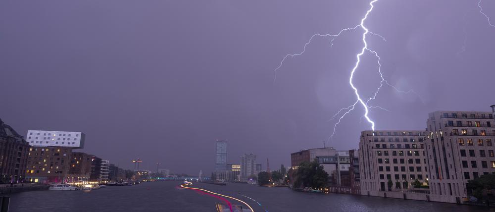 Ein Blitz entlädt sich am späten Abend über der Spree in Richtung Elsenbrücke am Himmel. 
