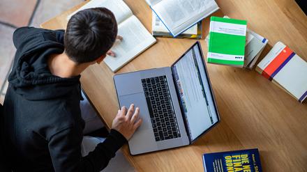 Ein Student arbeitet zu Hause am Laptop. Bücher liegen im Halbkreis drumherum.