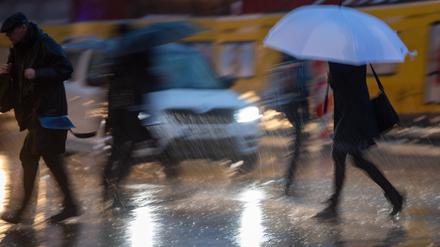 Passanten mit Regenschirmen gehen im Regen über die Straße. 