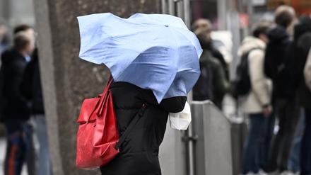 Ein Schirm fliegt einer Dame sturmbedingt um den Kopf.