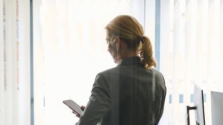 Eine Frau steht in einem Bürozimmer und hält ein Smartphone in der Hand. 