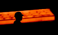 Die Silhouette eines Stahlarbeiters zeichnet sich im Werk der Salzgitter AG vor einer glühenden Bramme ab.