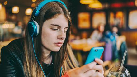 Young girl with headphones at cafeteria listening podcast