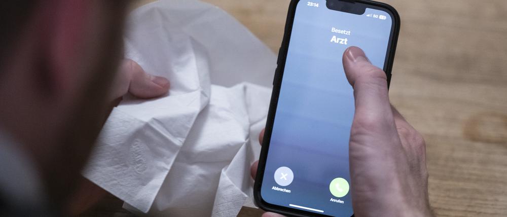 Ein Mann hält ein Taschentuch in einer Hand und ein Telefon mit dem Schriftzug „Arzt“ in der anderen. 