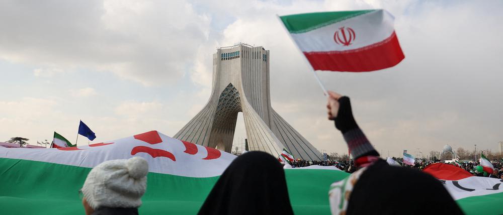 Menschen schwenken Flaggen vor einem Turm in Teheran.