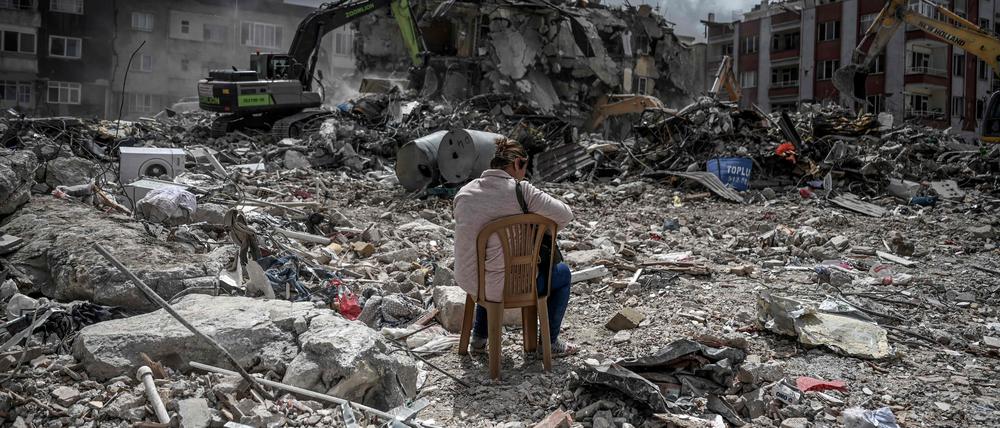 Eine Frau sitzt auf einem Stuhl in der Nähe ihres Hauses, während die Trümmer der eingestürzten Gebäude beseitigt werden.