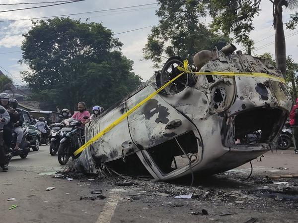 Rollerfahrer fahren an den Trümmern eines Autos vorbei, das bei Zusammenstößen zwischen Fußballfans nach dem Erstliga-Spiel zwischen Arema FC und Persebaya FC zerstört wurde. 
