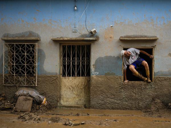 Ein Mann springt aus seinem Haus, das im Zuge eines Erdrutsches von Überschwemmungen getroffen wurde. 