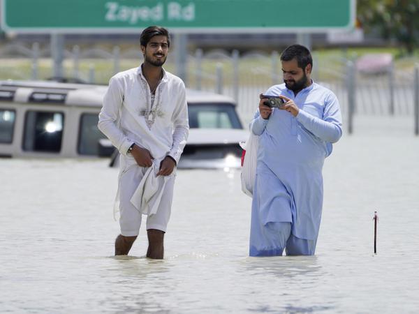 Zwei Männer waten durch eine überflutete Straße in Dubai.  Sie mussten ihre Autos zurücklassen.