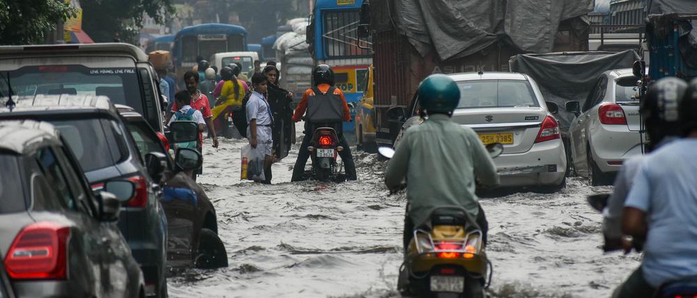 Indien, Kolkata: Menschen bahnen sich nach heftigen Regenfällen zu Fuß, in ihren Autos und auf Mopeds den Weg über eine überflutete Straße der Stadt.