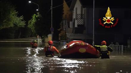 Feuerwehrleute schieben am 16.09.2022 ein Schlauchboot durch eine überflutete Straße in Senigallia, Italien.