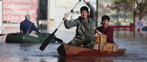 Zwei Männer rudern ein Boot durch das Hochwasser eines überschwemmten Gebiets.