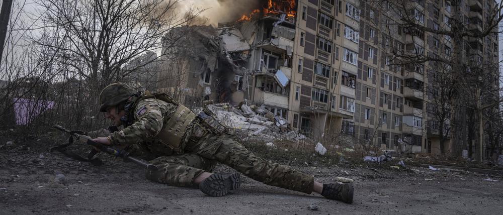Ein ukrainischer Polizist geht vor einem brennenden Gebäude in Deckung, das bei einem Luftangriff getroffen wurde. 