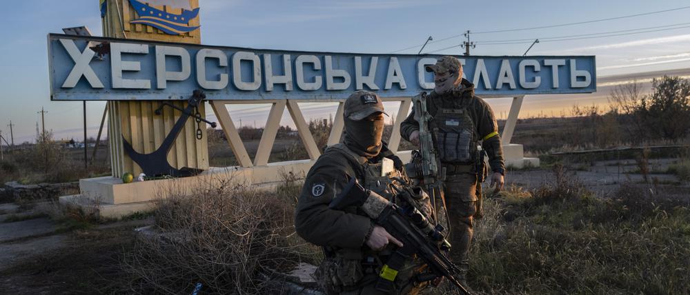 Zwei Mitglieder der ukrainischen Verteidigungskräfte stehen neben einem Schild mit der Aufschrift „Region Cherson“ am Stadtrand. 