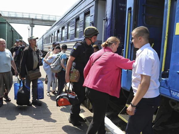 Menschen besteigen einen Evakuierungszug an einem Bahnhof.