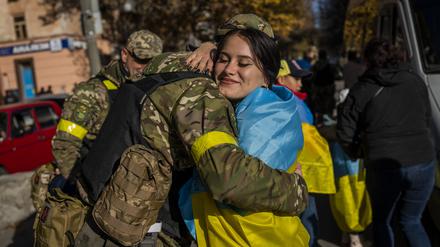 Eine Frau, die sich in eine ukrainische Fahne gewickelt hat, umarmt ein Mitglied der ukrainischen Verteidigungskräfte.