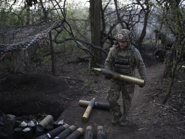 Ein ukrainischer Soldat trägt eine Granate für eine Haubitze an der Front.