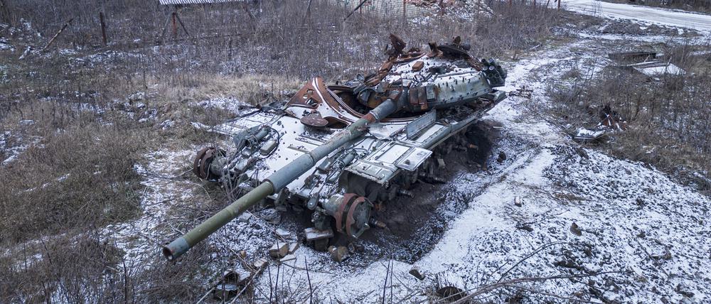 Ein zerstörter russischer Panzer, der von Schnee bedeckt ist, steht neben einer Straße.