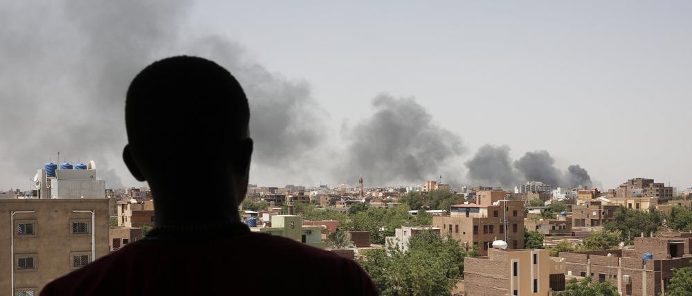 Ein Mann blickt auf die Stadt Khartum, wo schwarzer Rauch aufsteigt.