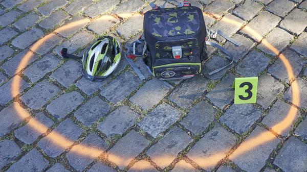 Helm und Ranzen auf dem Boden: nachgestellte Situation eines Verkehrsunfalls.