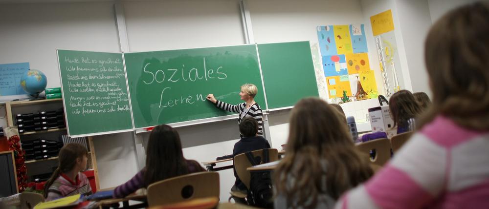 Eine Lehrerin schreibt in einer Klasse an der Tafel.