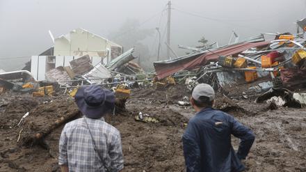 Menschen schauen auf ihre eingestürzten Häuser nach einem durch starken Regen verursachten Erdrutsch. 