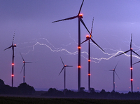 Ein Blitz erhellt den Nachthimmel über Windenergieanlagen mit roten Positionslichtern.