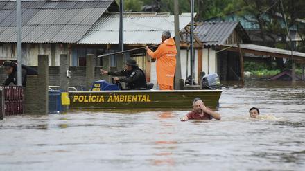 Polizeibeamte kontrollieren ein Haus, während Anwohner über eine überschwemmte Straße im Bundesstaat Rio Grande do Sul waten, nachdem ein Unwetter Überschwemmungen verursacht hat. Bei schweren Unwettern im Süden Brasiliens sind mindestens 36 Menschen ums Leben gekommen. 