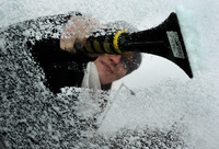 Tipps für eisfreie Autoscheiben: Eine Autofahrerin kratzt Eis von der Windschutzscheibe eines Fahrzeuges.