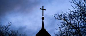Dunkle Wolken ziehen über das Kreuz auf einer evangelischen Kirche in der Region Hannover hinweg.