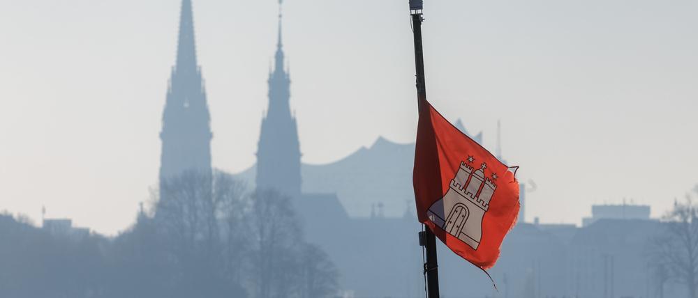 Die Hamburg-Fahne weht am 17.12.2022 vor dem winterlich diesigem Panorama von Nikolaikirche, Rathausturm und Elbphilharmonie.